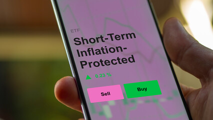 An investor's analizing the short-term inflation-protected securities etf fund on a screen. A phone shows the prices of short term inflation protected Securities