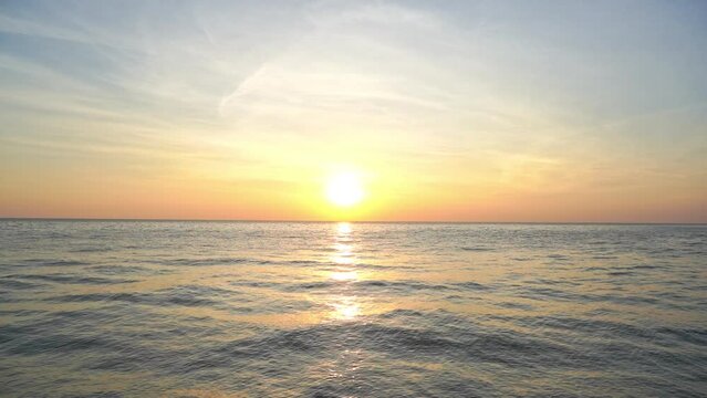 Beautiful sunset over sea with sun near horizon, sunsilght reflection on moving waves