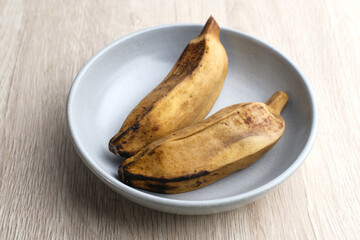 Pisang Kukus or Steamed Banana, Indonesian traditional food, a healthy snack. Served in small bowl on wooden table. Close up.
