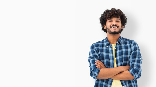 Young Indian male student smiling joyfully standing on a white background. Asian man in casual clothes with curly hair and happy smile