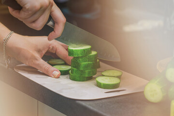 The cook in the kitchen at work prepares a vegetable salad and cuts a green cucumber. The girl is engaged in slicing cucumbers on a cutting board. A woman cuts vegetables for a salad. 