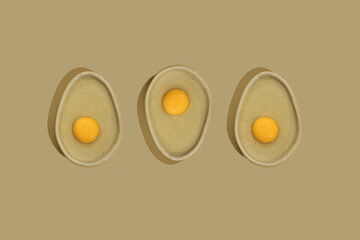 Three avocado shaped ceramic plate with yellow raw egg yolk on a bright beige color background with copy space. Healthy dieting idea.