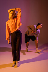 Pretty woman touching hair near boyfriend on purple background with lighting.