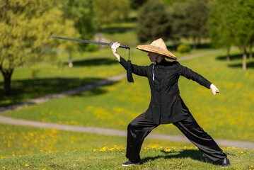 Asian woman with sword practicing taijiquan outdoors, chinese martial arts, healthy lifestyle...