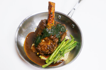 slow cooked lamb hind shank with potato and green beans in metal plate
