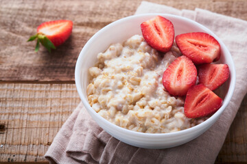 Oatmeal. Bowl of oatmeal porridge with strawberry, almond and milk on old wooden dark table background. Top view in flat lay style. Natural ingredients. Hot and healthy breakfast and diet food.