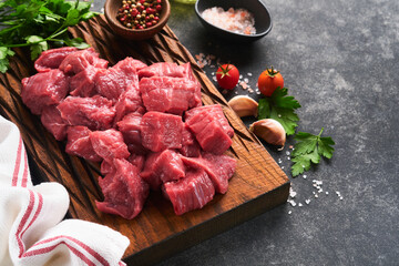 Raw chopped beef meat. Raw organic meat beef or lamb, spices, herbs on old wooden board on dark grey concrete background. Goulash. Raw uncooked meat. Meat with blood. Top view with copy space.