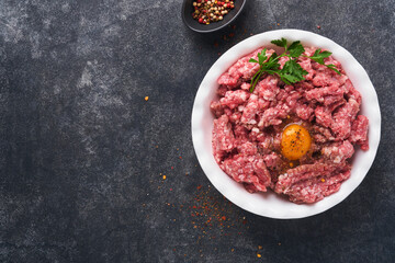 Raw minced meat. Ground meat beef, pork or lamb spices, herbs and eggs on white plate on black old concrete background. Fresh minced meat ready for cooking. Food cooking background. Top view.
