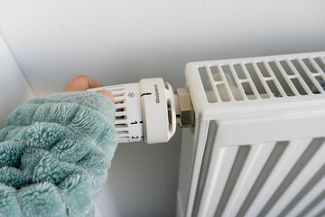 Person mit decke schaltet Thermostat auf Heizung herunter, um Energie zu sparen.