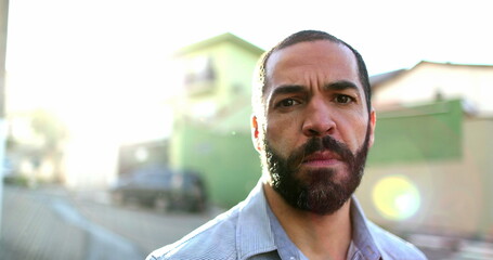 Serious hispanic man standing outside in street looking at camera