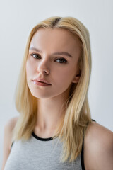 Fototapeta premium Portrait of blonde woman in top looking at camera isolated on grey.