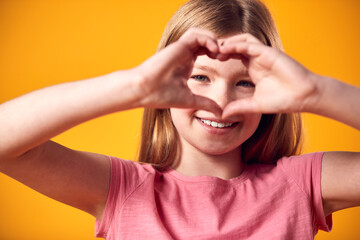Studio Portrait Of Smiling Girl Making Heart Shape With Hands Against Yellow Background