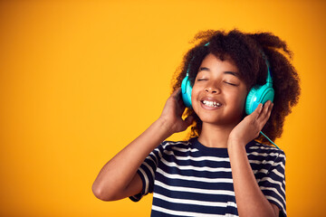 Studio Shot Of Smiling Young Boy Listening To Music On Headphones Against Yellow Background