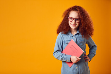 Fototapeta premium Studio Portrait Of Young Girl With School Exercise Book Wearing Glasses Against Yellow Background