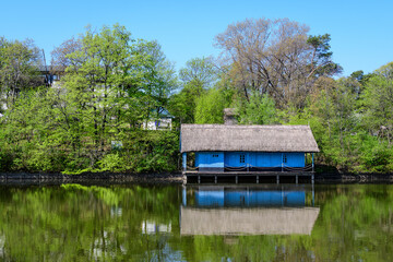 Fototapeta premium Landscape with old blue house and many large old green trees trees on the shoreline of Herastrau Lake in King Michael I Park in Bucharest, Romania, in a sunny spring day with blue sky.