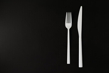 White fork and knife on the black background.