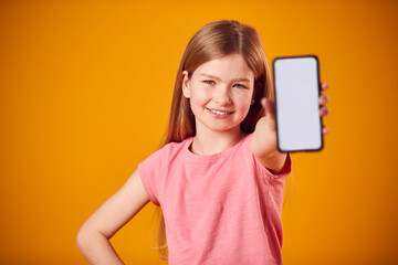 Naklejka premium Studio Portrait Of Girl Showing Mobile Phone With Social Media Screen Against Yellow Background