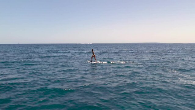 4k SlowMo - Aerial view of a young woman surfing on a motorized board on the beautiful beaches of crystal clear turquoise water in Ibiza