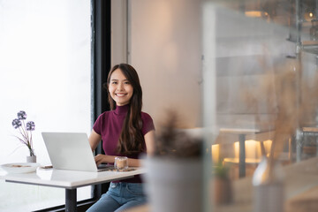 Young Asian woman using laptop in coffee shop and looking at camera.