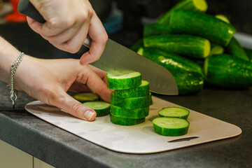 The cook in the kitchen at work prepares a vegetable salad and cuts a green cucumber. The girl is engaged in slicing cucumbers on a cutting board. A woman cuts vegetables for a salad. 