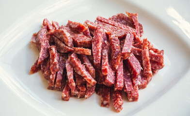 Lots of Spanish Serrano ham and Spanish sausage, festive, Iberian pork loin on a white platter. Smoked sausage cut into small slices in a white plate close-up selective focus.  Meat products.