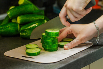 The cook in the kitchen at work prepares a vegetable salad and cuts a green cucumber. The girl is engaged in slicing cucumbers on a cutting board. A woman cuts vegetables for a salad. 