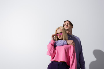 Man in purple sweatshirt embracing girlfriend in sunglasses on grey background.