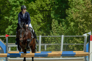 A young woman performs a sports race on a horse on a sunny summer day.