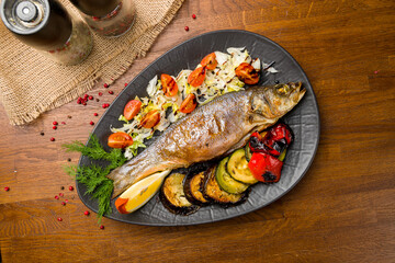 Fried sea bass with grilled vegetables on black plate
