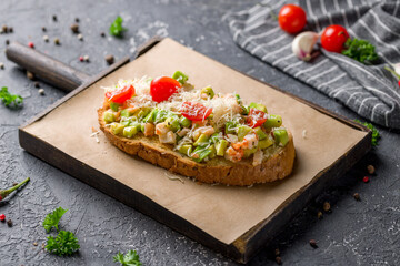 Bruschetta with prawns, avocado,tomatoes and parmesan on the board on grey table