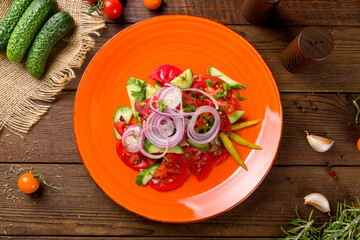 Vegetable salad with tomatoes, cucumbers and red onion on wooden table