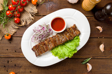 skewers of mutton flesh and tomato sauce with red onion on plate on wooden table