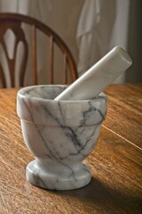 Close-up of marble mortar and pestle standing on a wooden tabletop side lit by sunny window with...