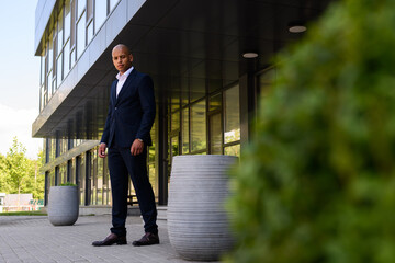 Young african american businessman in suit looking at camera near building on urban street 