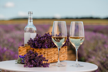 Two Glasses of white wine and bottle in a lavender field in Provance. Violet flowers on the...