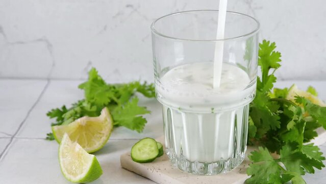 Fresh asian yogurt drink kefir, ayran in glass with smashed herbs. Ayran, homemade summer healthy cocktail with herbs, lime, cucumbers. Probiotic, postbiotic fermented dairy drink