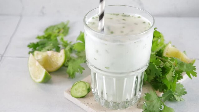 Fresh asian yogurt drink kefir, ayran in glass with smashed herbs. Ayran, homemade summer healthy cocktail with herbs, lime, cucumbers. Probiotic, postbiotic fermented dairy drink