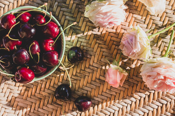 Cherries and roses on a rattan table in the sunshine. Summer country background