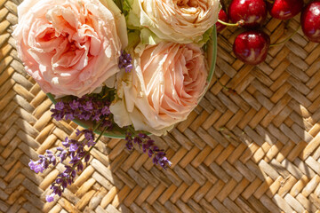 A romantic bouquet of roses and cherry fruits on the table. The rays of the setting sun. Slow living, summer in countryside. Atmospheric tranquil moment. Enjoy slow life. Top view.