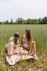 Man touching belly of pregnant wife on blanket in field.