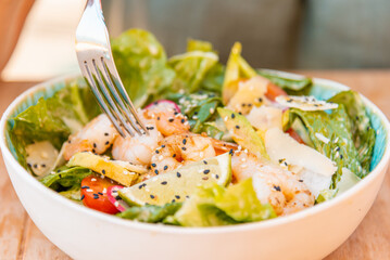Healthy salad plate. Part woman hand and fork.Fresh summer salad with shrimp, avocado and tomato in bowl on light table. Grilled shrimps and fresh vegetable salad.Healthy food.