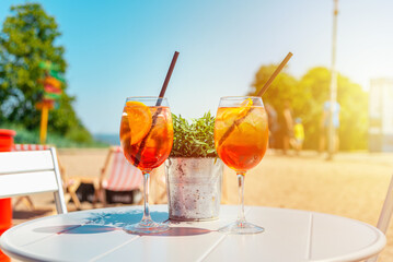 Two glasses of orange spritz aperol drink cocktail on table outdoors sunset with sea and trees view blurred background.
