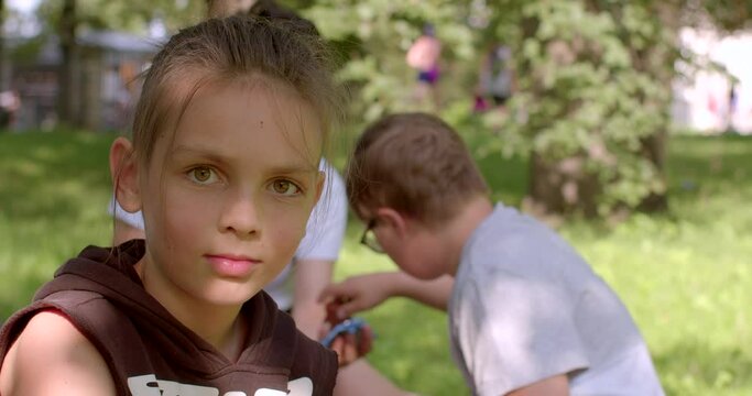 Portrait of a teenager in a city park. He looks into the camera. Sunlight falls on the face. Against the background, friends in bokeh, biting food, communication.