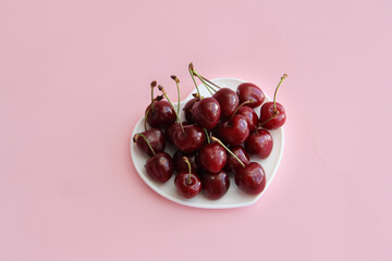 A lot of cherries on a white plate in the form of a heart on a pink background