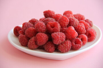 large ripe raspberries in a white plate on a pink background