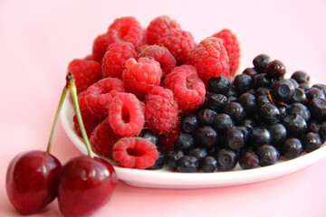 ripe raspberries and blueberries on a white plate in the shape of a heart on a light background close-up