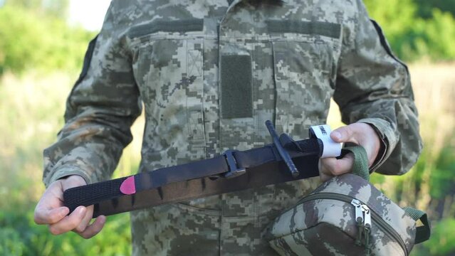 a military man in uniform holds a tourniquet in his hands, preparing it for use. combat medicine, training of combat medics. stopping massive bleeding. medics on the battlefield. first aid