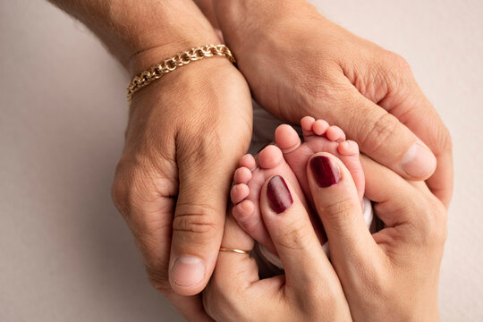 The palms of the parents. A father and mother hold the feet of a newborn child on a white studio background.. The feet of a newborn in the hands of parents. Macro Photography of foot, heels and toes.