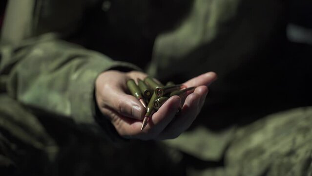 a soldier gathers bullets for a machine gun in his hand at night, preparing for battle. ammunition count close-up. weapon loading. evening check of ammunition. military man in uniform