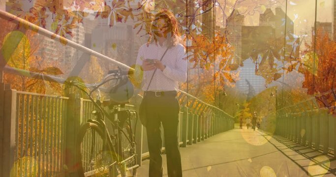 Animation of autumn leaves falling over caucasian man with bike using smartphone